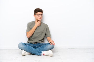 Teenager Russian man sitting on the floor isolated on white background with glasses and smiling