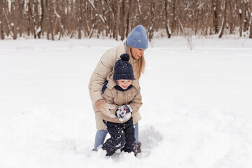 Fototapeta na wymiar Portrait of young woman with her adorable little toddler boy on a winter cold day. Mother and child walking in the park. Happy family outdoors. Winter, Christmas and lifestyle concept