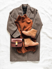 Seasonal women's clothing - coat, cashmere sweater, suede boots, crossbody bag on a light background, top view