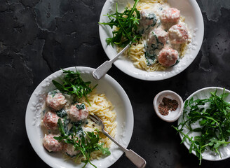 Risoni pasta with salmon meatballs in cream sauce with spinach and arugula - a delicious lunch on a dark background, top view