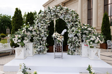 Wedding ceremony outdoor. A beautiful and stylish wedding arch, decorated by various fresh white flowers, standing in the garden. Celebration day.