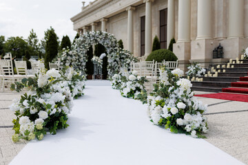 Wedding ceremony outdoor. A beautiful and stylish wedding arch, decorated by various fresh white flowers with white chairs, standing in the garden. Celebration day.