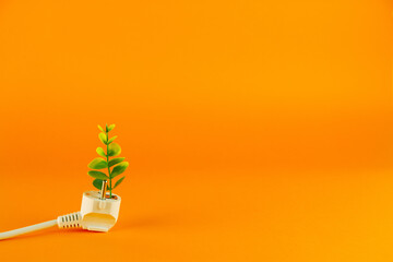 Green energy concept with plug and plant on orange background with copy space