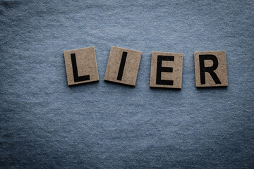 The word liar formed with wooden blocks on a blue fabric. - obrazy, fototapety, plakaty