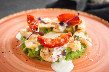 A delicate arrangement of shrimp on pesto-like green puree with cream sauce, presented on a coral plate with a minimalist black background