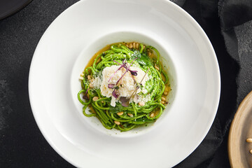 Elegantly plated pesto spaghetti with creamy stracciatella cheese and toasted pine nuts, served in a white bowl on a sleek black surface