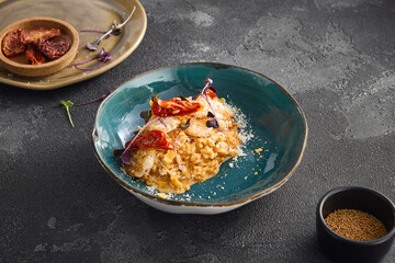 Creamy shrimp risotto adorned with sun-dried tomatoes, served in a stylish bowl, part of a minimalist table setting on a dark background