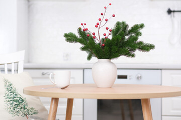 Christmas kitchen interior - ceramic vase with fur branches, ceramic christmas tree, cup of tea on round wooden table in light kitchen. 