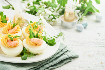 Stuffed or deviled eggs yolk, shrimp, pea microgreens with paprika for easter table decorate fresh cherry or apple blossoms on white light background. Happy Easter traditional dish concept. Mock up.