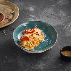 Creamy shrimp risotto adorned with sun-dried tomatoes, served in a stylish bowl, part of a minimalist table setting on a dark background