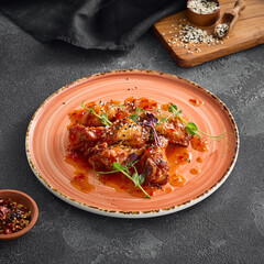 Crispy fried chicken wings doused in a luscious sweet chili sauce, delicately placed on a round ceramic plate, accentuated by a dark background