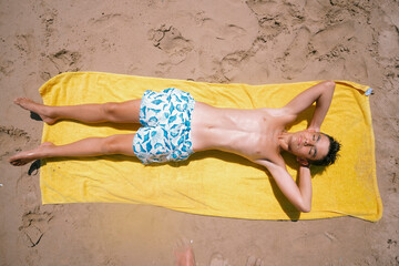 Teenage boy lying on the towel on a fabulous day at the beach.