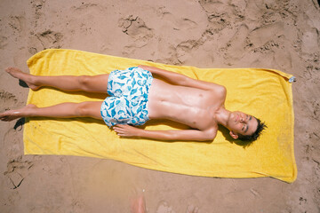 Teenage boy lying on the towel on a fabulous day at the beach.