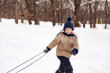 Fototapeta na wymiar happy joyful beautiful child boy rides from the mountain on a sled in winter. Little boy goes to ride down slide in winter. Winter time outdoor