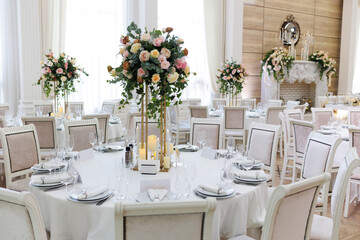 Wedding decorations. Served wedding table with decorative fresh white and pink flowers, candles. Celebration details. Flower composition roses, plates, candles in candlesticks 