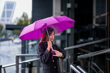 Caucasian girl, brown hair, black jacket, rain, purple umbrella, waiting in Madrid.