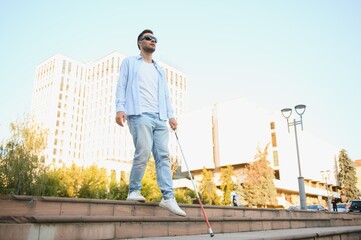 Young handsome blinded man walking with stick in town