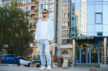 Fototapeta na wymiar Young handsome blinded man walking with stick in town
