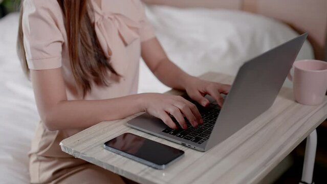 Medium Shot, asian female hands typing on laptop computer placed on table, type quickly fluently with work do, women work at home, hand picks up coffee cup drinks while working.