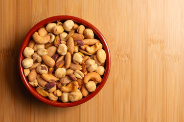 Mixed nuts in bowl on wooden background, top view. Roasted, peeled, salted peanuts, hazelnuts, cashews, almonds, pistachios. Free text space on wooden background.