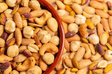 Mixed nuts in bowl in selective focus and out of focus, top view. Roasted, peeled, salted peanuts, hazelnuts, cashews, almonds, pistachios.