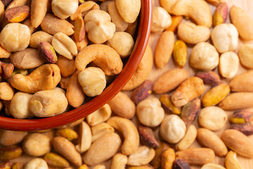 Mixed nuts in bowl in selective focus and out of focus, top view. Roasted, peeled, salted peanuts, hazelnuts, cashews, almonds, pistachios.