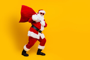 Side photo of pensioner man steps santa claus sack wearing red costume overweight person celebrate xmas isolated on yellow color background