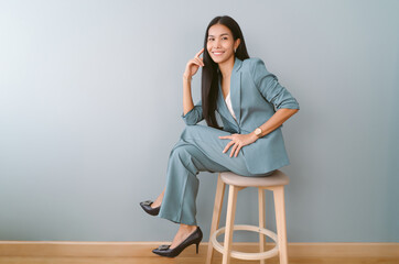 Portrait of beautiful Asian business woman sitting on chair and looking away posing on green pastel background, Full length photo.