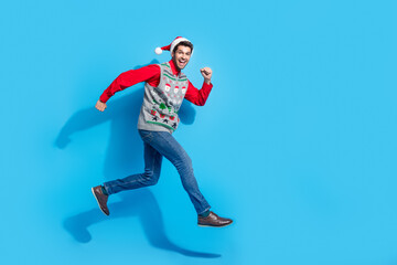 Full length photo of nice young male running fast have fun hurry wear x-mas print vest hat garment isolated on blue color background