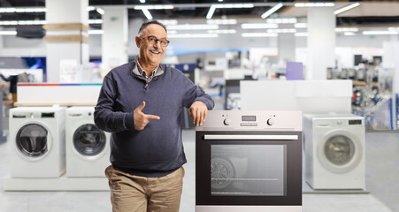 Mature man leaning on an oven and pointing inside a kitchen and home appliances store