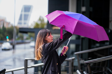 Stylish girl, brown hair, rain, Madrid skyline, opening colorful umbrella, urban scene.