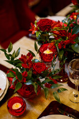 Wedding decorations. Served wedding table with decorative fresh red flowers and candles. Celebration details. Flower composition roses plates and candles in candlesticks