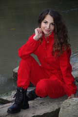 Portrait of an attractive, pretty woman in red overalls, posing on a stone in the river