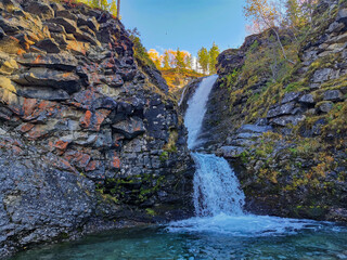 A beautiful waterfall in the autumn mountains beyond the Arctic Circle in the north, in Khibiny, Murmansk region. Panoramic view of a beautiful waterfall in the mountains in autumn, Kola Peninsula