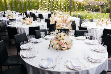 Black chairs and tables decorated white white plates and natural purple and white flowers and reed,...