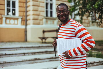 Authentic portrait of young successful African American man wearing stylish eyeglasses, standing on the street. Handsome asian model posing for pictures, looking at camera, smiling