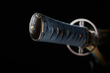 Antique hilt of a Japanese katana sword with a blue binding and chasing on a black background