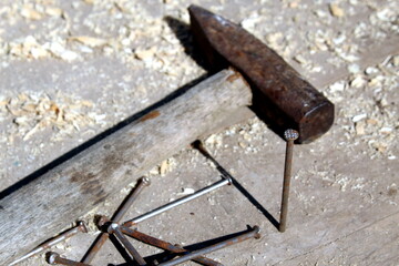 An old hammer lies with rusty nails on a wooden board.