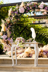Close up of a table decorated with fresh purple and green flowers for painting the newlyweds against the backdrop of the arch. Wedding concept