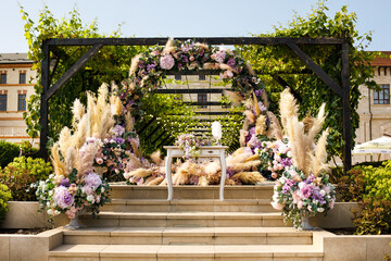 A round arch for the painting of the newlyweds decorated with greenery, violet, pink and dried...