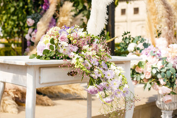 Close up of a table decorated with fresh purple and green flowers for painting the newlyweds against the backdrop of the arch. Wedding concept