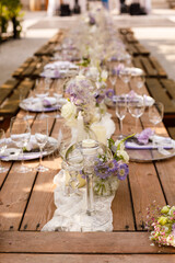 Wedding decorations. Set wedding table with silver plates, purple napkins, decorative fresh and dried flowers, candles and light bulbs. Celebration details, outdoor wedding