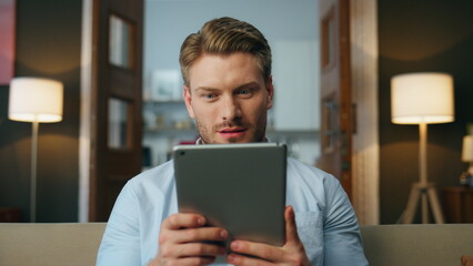 Inspired businessman reading tab home zoom on. Laughing man tablet funny video