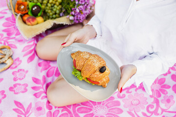 Female hands holding a plate with fresh croissant in nature in summer