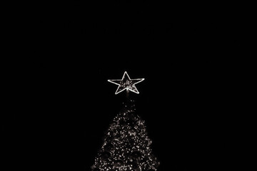 Black and white closeup of a star tree topper on top a giant Christmas tree lit up with string...
