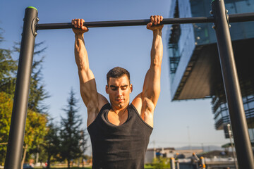 One man muscular male athlete training pull ups outdoor in sunny day