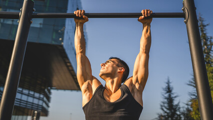 Naklejka premium One man muscular male athlete training pull ups outdoor in sunny day