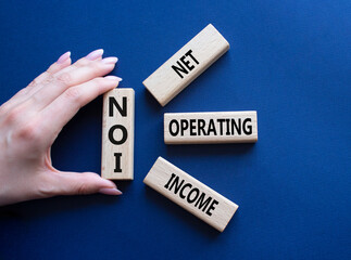 NOI - Net Operating Income symbol. Concept word NOI on wooden cubes. Businessman hand. Beautiful deep blue background. Business and NOI concept. Copy space.