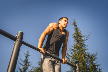 One man muscular male athlete training pull ups outdoor in sunny day