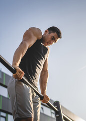 One man muscular male athlete training pull ups outdoor in sunny day